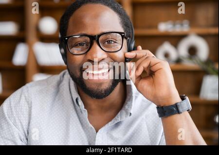 Webcam view of cheerful African American young businessman in a headset holding the microphone, attentive male customer service representative responding to the customer inquiry Stock Photo