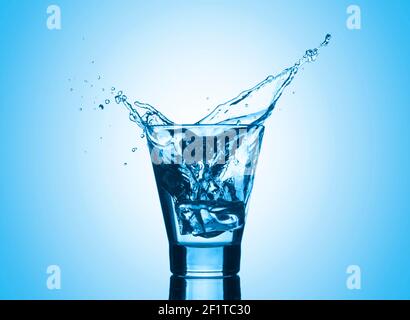 Water with splash and ice on blue background. Mineral water with ice in a glass. Stock Photo