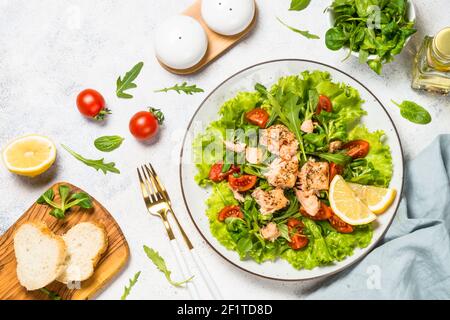 Green salad with baked fish at white table. Stock Photo