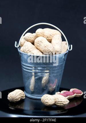 Red peanut seeds in miniature bucket on black background. Stock Photo