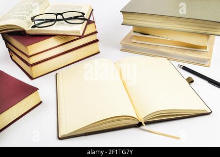 Open notebook with stack of books in background. Selective focus. Stock Photo