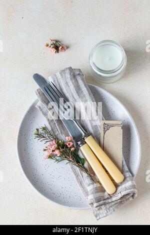 Romantic or spring table setting. Knife and fork, little pink flowers and linen napkin on a plate, light concrete background. Flat lay. Selective focu Stock Photo