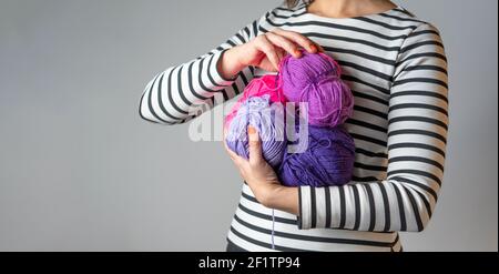 Woman with striped T-shirt and orange nail polish holding some purple and pink balls of wool with copy space Stock Photo