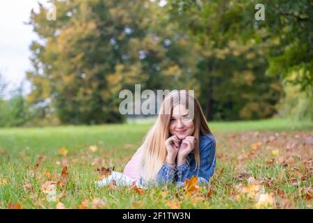 A young girl lies on the grass in a warm autumn in the evening with a petal in her hands. Stock Photo