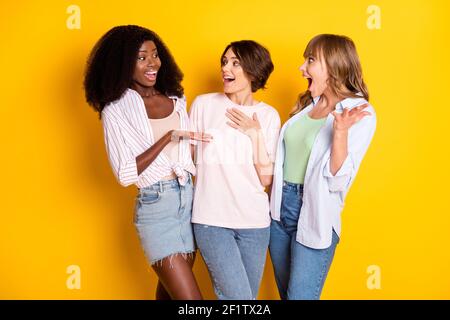 Portrait of three attractive cheerful girls talking having fun gossiping embracing isolated over bright yellow color background Stock Photo