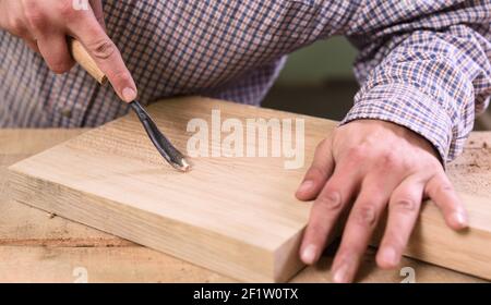 Carpenter hands working on wooden board with chisel closeup Stock Photo