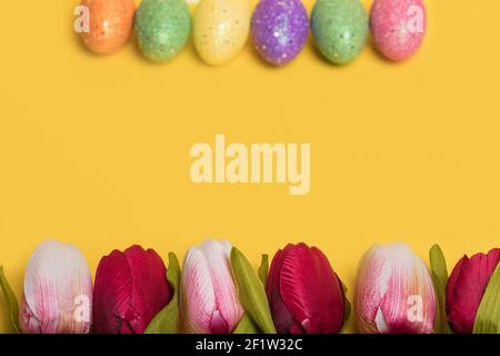Creative Easter frame made of colorful eggs and tulips on illuminating yellow background. Minimal easter concept. Easter card with copy space for text Stock Photo