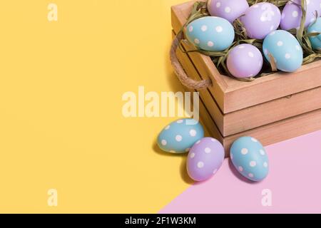 Easter colored eggs in a basket isolated on a trendy illuminating yellow and pastel pink background. Minimal easter concept. Easter card with copy spa Stock Photo