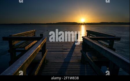 Wooden jetty with benches on a frozen lake in the light of the golden rising sun, beautiful landscape scenery, concept for a new beginning every day, Stock Photo