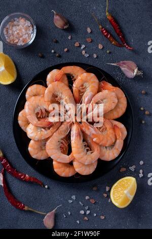 Boiled shrimps in a round plate and spices on a dark background. Vertical format Stock Photo