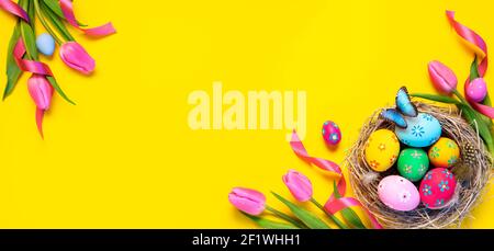 Easter - Colorful Eggs In Nest With Butterfly And Pink Tulips In Yellow Background Stock Photo