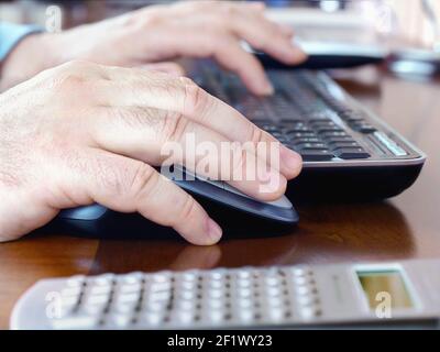 Man's hands on computer mouse and keyboard Stock Photo