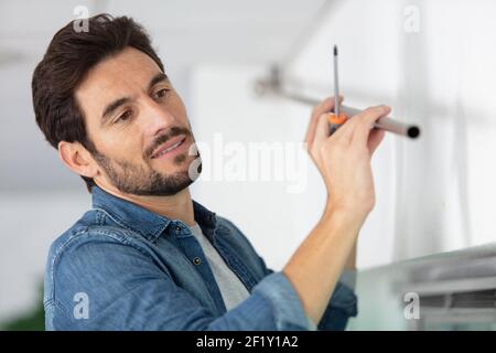 male builder installs curtain on ceiling indoors Stock Photo