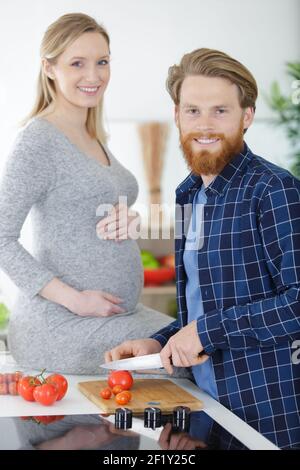 happy pregnant woman and her husband mixing vegetables Stock Photo