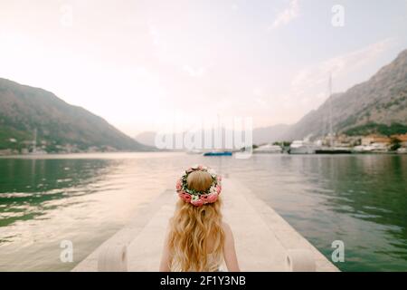 A bride in a delicate wreath of roses stands on a pier near Kotor in the Bay of Kotor, back view  Stock Photo