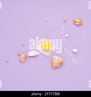 Cracked egg, eggshell with yolk isolated on purple background. Broken idea concept. Stock Photo