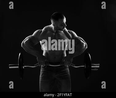 Muscular strong men, athlete, bodybuilder, weightlifter does exercises with barbell for top and arms, looking at it Stock Photo