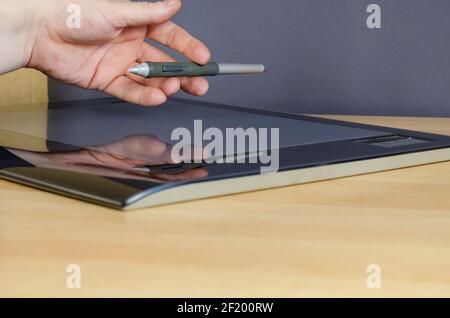 A man's hand with a special pen on top of the screen of a graphics tablet. A professional device for designers lying on a table. Side view from an ang Stock Photo