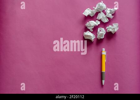 Pen and scraps of crumpled paper balls on a pink background with shadows. Yellow plastic pen and scraps of white paper. Top view at an angle. Copy spa Stock Photo
