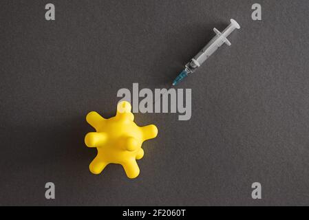 Syringe and yellow coronavirus shape toy ball on grey background. Vaccine covid-19 virus protection concept. Stock Photo