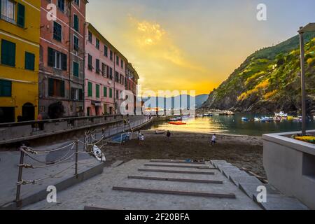 Children play along the sandy beach of Vernazza Italy harbor on the Cinque Terre as tourists enjoy a sunset dinner along the pier.