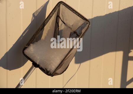 fishing or landing net covered with fresh white snow at winter time in front of dirty metal wall Stock Photo