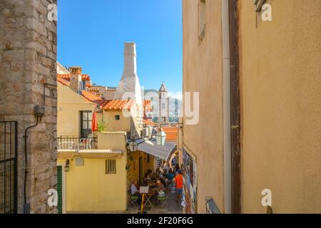 Tourists enjoy a meal at a sidewalk cafe on one of the narrow alleys inside the ancient wall of the city of Dubrovnik, Croatia. Stock Photo