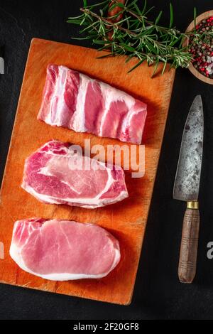Pork meat types, different cuts, top shot on a black background with rosemary, pepper, and a knife Stock Photo