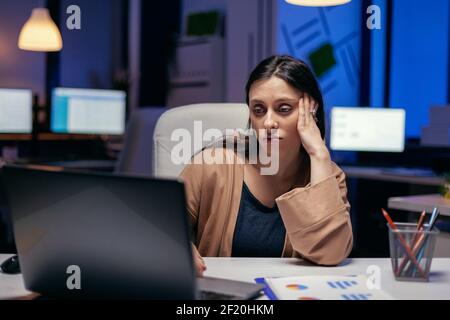 Tired entrepreneur trying concentrate looking at how much work has to be done for a deadline. Smart woman sitting at her workplace in the course of late night hours doing her job. Stock Photo