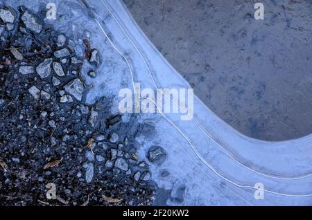 Frozen water in a puddle on the ground with abstract structures and surface, view from directly above Stock Photo