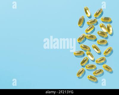 Vitamin D3, Omega or Evening Primrose Oil gel capsules on blue background. Top view or flat lay yellow liquid capsules with nutritional supplement oil. Copy space for text. Stock Photo
