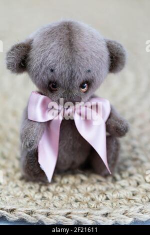 A cute toy teddy bear with a pink bow sits on a wicker background Stock Photo