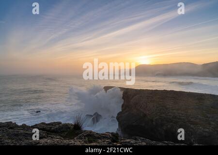 A view of huge storm surge ocean waves crashing onto shore and cliffs at sunrise Stock Photo