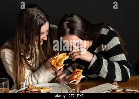 girl give a slice of pizza to another girl while she can't stop laughing Stock Photo