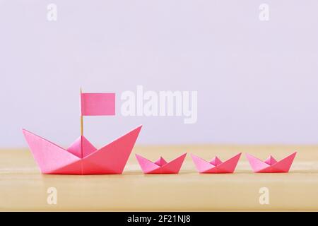 Pink paper boat with flag and three small paper boat - Concept of women's leadership and teamwork Stock Photo