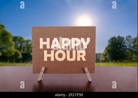 Happy hour text on card on the table with sunny green park background. Stock Photo