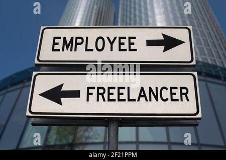 Employee versus freelancer road sign with two arrows on business skyscraper background. White two street sign with arrows on metal pole. Stock Photo