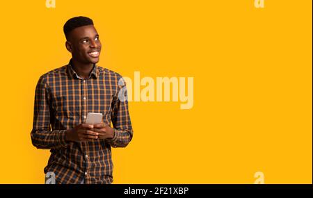 Mobile Offer. Excited Cheerful Black Guy Holding Smartphone And Looking Aside Stock Photo