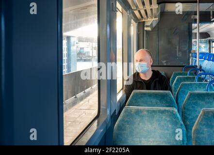 Serious man wearing surgical mask looking through the window in a train Stock Photo