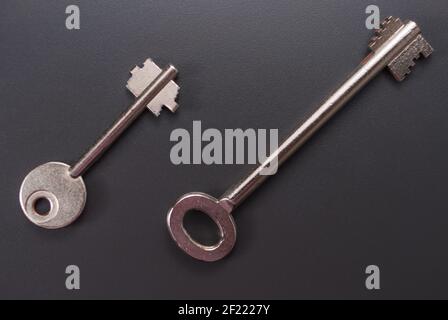One small and one full-size safe key, safe keys on a dark background and a large open space