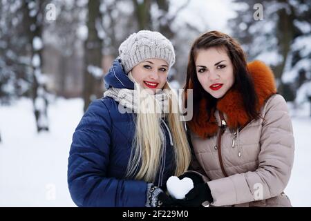 Two girlfriends holding a heart made of snow on valentine's day Stock Photo