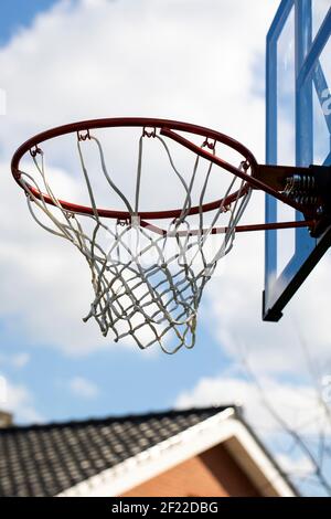 A portrait of an outdoor basketball rim with a net and a plexiglass backboard with blue lines on it in front of a cloudy sky. The basketball hoop or r Stock Photo