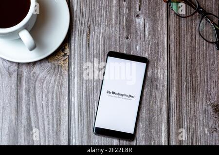 A mobile phone or cell phone laid on a wooden table with the Washington Post app open on screen next to a coffee Stock Photo