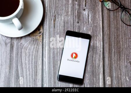 A mobile phone or cell phone laid on a wooden table with the DuckDuckGo app open on screen next to a coffee Stock Photo