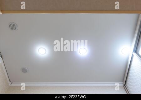 Stretch white matte ceiling in the hallway, ventilation grilles and spotlights are installed in the ceiling Stock Photo