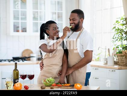 Cheerful black couple cooking and tasting healthy food in kitchen at home Stock Photo