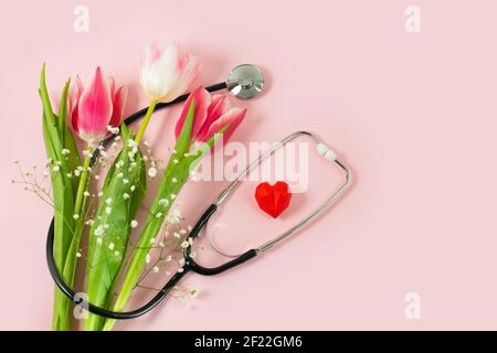 Bunch of pink tulips and stethoscope with red hearts on pink background. Happy nurse day. National Doctors day. womens health. flat lay top view, Stock Photo