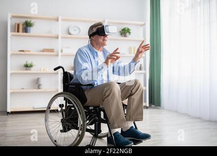 Happy handicapped senior man in wheelchair using VR headset to explore augmented reality at home Stock Photo