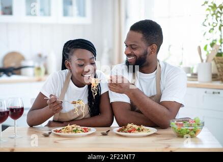 African American Lovers Eating Spaghetti And Drinking Red Wine In Kitchen Stock Photo