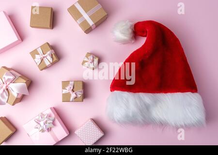 Santa Claus hat with Christmas gift boxes on pastel pink backdrop. Minimal Christmas or New Year concept. Stock Photo